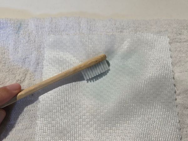 歯ブラシでカーテンの端切れを掃除している
