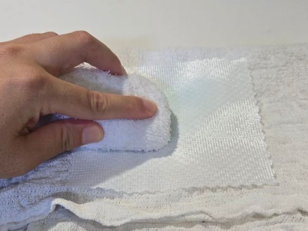 濡れタオルでカーテンの端切れの洗剤を落としている