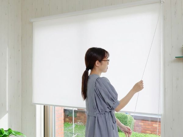 正面付けのロールスクリーンを操作する女性