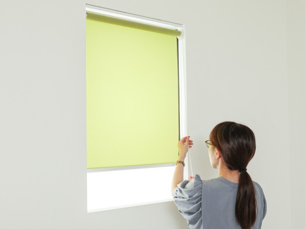 天井付けのロールスクリーンを操作する女性