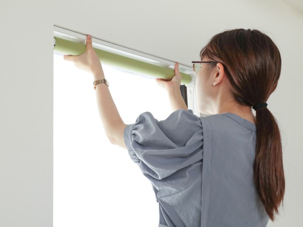 ロールスクリーンを天井付けしている女性